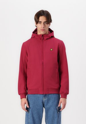 Rode zip-up hoodie met een gestructureerde afwerking, voorzien van een capuchon en zijzakken, en een klein groen logo op de borst. Gecombineerd met lichtblauwe jeans.