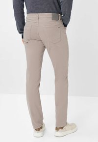 Beige Slim-Fit-Hose aus einem Baumwollmix, mit Gesäßtaschen und einem Logo-Patch am Bund, kombiniert mit lässigen weißen Sneakern.