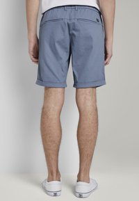 Pantalones cortos informales azules de mezcla de algodón, con dobladillos enrollados, dos bolsillos traseros y una cinturilla elástica para mayor comodidad. Combinados con zapatillas blancas.