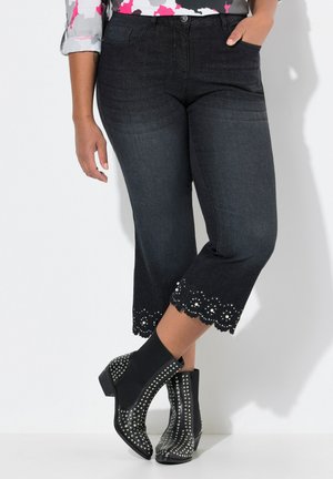 Pantalones capri de mezclilla oscura con dobladillo ondulado y perlas decorativas. Combinados con botas de tobillo negras adornadas con tachuelas plateadas.