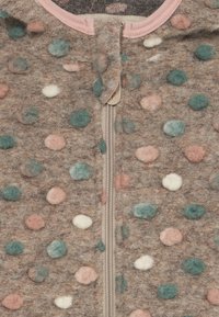 Tissu brun duveteux avec des pois roses, verts et blancs, présentant une fermeture éclair beige centrale et une bordure rose au niveau du col.