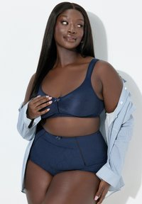 Laivastonsininen rintaliivi ja korkeavyötäröiset alushousut teksturoidusta kankaasta. Rintaliivissä keskellä pieni rusetti; alushousuissa hienovarainen kuvio ja saumadetaljit.