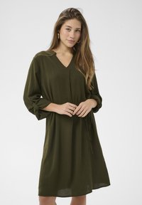 Olivno zelena obleka do kolen iz lahkega blaga z V-izrezom, rokavi tri četrtine in detajlom na pasu s kravato. Skladen, gladek tekst.