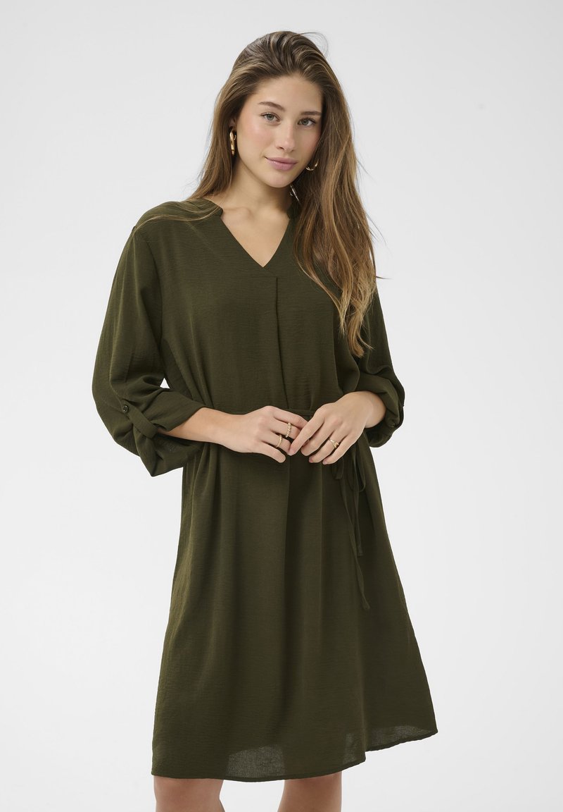 Olivno zelena obleka do kolen iz lahkega blaga z V-izrezom, rokavi tri četrtine in detajlom na pasu s kravato. Skladen, gladek tekst.