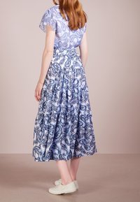 Robe bleue à motif cachemire avec jupe à volants et manches courtes transparentes. Portée avec des baskets blanches, affichant un style décontracté et relax.