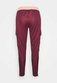 Bordeauxkleurige cargobroek met een elastische roze tailleband, twee zijzakken en een taps toelopende pasvorm, gemaakt van een gladde, stretchy stof.