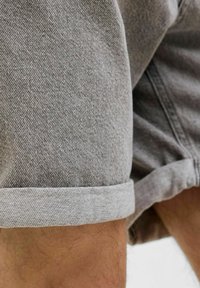 Shorts en denim gris avec un ourlet replié, présentant une texture subtile et une coupe droite. Un gros plan met en évidence le tissage du tissu et les coutures.