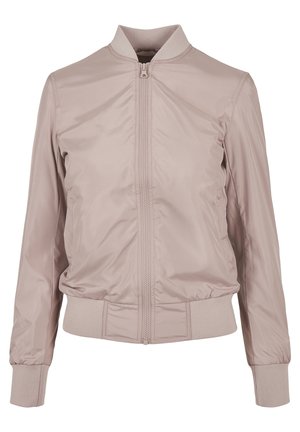 Woman wearing light pink bomber jacket, white cropped t-shirt, matching wide-leg pants, and white sneakers, standing with hands in pockets.