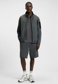 Grijze ritsjack met een textuurpatroon, gecombineerd met een bijpassend grijs t-shirt en shorts, afgerond met grijze en witte sneakers.