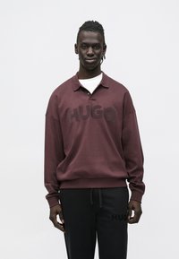 Bordeauxfarvet sweatshirt med polokrave og fedt "HUGO"-logo på tværs af brystet, kombineret med sorte joggebukser med et subtilt logodetalje.
