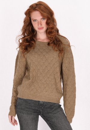 Khakifarbener Pullover mit Rautenmuster, geripptem Halsausschnitt und Bündchen. Getragen mit dunkelgrauen Jeans. Der Stoff wirkt strukturiert und gestrickt.