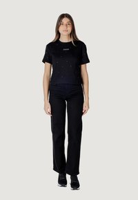 T-shirt nera corta con decorazioni in argento, abbinata a pantaloni neri a gamba dritta e sneakers nere, su uno sfondo neutro.