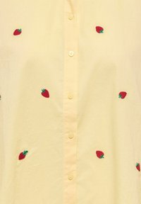 Chemise jaune à boutons avec de petites fraises rouges brodées, réparties uniformément sur le tissu.