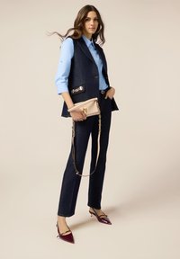 Chaleco de mezclilla navy con herrajes dorados, camisa celeste, pantalones de mezclilla oscuros y tacones de charol burdeos tipo slingback. Bolsa beige con asa de cadena.