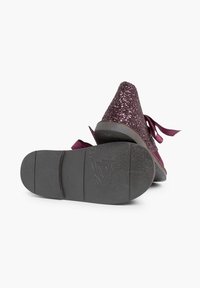 Zapatos de cuña morados con un upper brillante, cordones de cinta de satén y una suela de goma negra texturizada. La altura del tacón es moderada.
