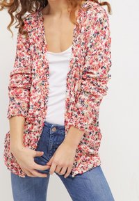 Stickad kofta med ett flerfärgat mönster i röd, rosa och vit. Den har långa ärmar, öppen front och en avslappnad passform.