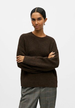 Maglione marrone lavorato a maglia con una vestibilità ampia, collo e polsini a costine, abbinato a pantaloni grigi a quadri con una silhouette rilassata.