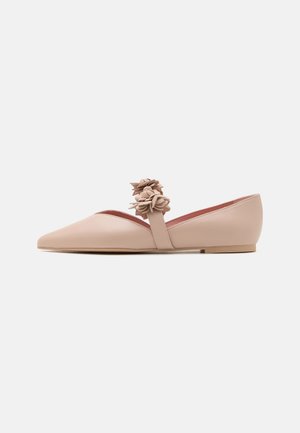 Beżowy, płaski but z noskiem w szpic, z paskiem na górze ozdobionym trzema dekoracyjnymi skórzanymi klastrami w kształcie kwiatów.