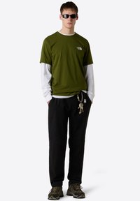 Vihreä lyhythihainen t-paita, jossa on valkoinen reuna, valkoisen pitkähihainen paidan päällä, mustat housut ja tummat lenkkarit; avaimet kiinnitetty vyötärölle.