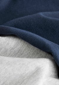 Kerangka kain dalam nuansa biru navy dan abu-abu muda, menunjukkan tekstur halus dan desain rajutan lembut dengan variasi halus dalam bayangan.