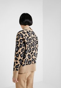Suéter de estampado de leopardo en tonos marrón y negro, con un cuello y puños acanalados, textura suave y un corte holgado, combinado con pantalones beiges.