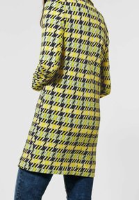 Mantello lungo con un audace motivo a pied-de-poule giallo, verde e nero. Realizzato in tessuto intrecciato con una vestibilità dritta e maniche lunghe.