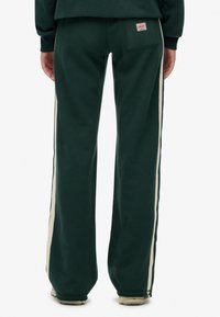 Groene sweatpants met crèmekleurige zijstrepen, met een achterzak en een zachte textuur. Ontspannen pasvorm, elastische tailleband en wijd ontwerp.