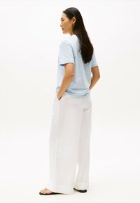 Jasnoniebieska bawełniana koszulka z krótkim rękawem w połączeniu z białymi, szerokimi spodniami. Prosty design, miękka tekstura i luźny krój.