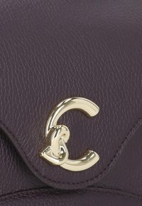 Borsa a tracolla in pelle viola con una chiusura a forma di C dorata, superficie testurizzata e dettagli di cucitura ordinata lungo i bordi.