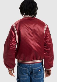 Veste bomber en satin rouge avec poignets et ourlet côtelés rayés. Dispose d'accents brodés sur les manches et d'une coupe décontractée.