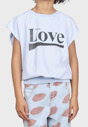 Barn iført en hvid ærmeløs trøje med teksten "Always Love" og lyseblå bukser med et pink abstrakt mønster.
