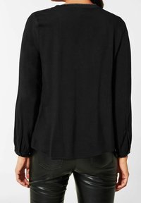 Svart långärmad topp med rundad halsringning, mjukt tyg och lätt rynkning vid ärmsluten. Har en avslappnad passform och slät yta.