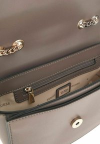 Sac à main gris clair avec une texture lisse, featuring un détail en chaîne dorée, un compartiment zippé et une doublure intérieure avec marque.