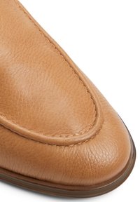 Tan leather loafer with a rounded toe, featuring subtle texture, contrasting stitching, and a smooth finish around the edge.