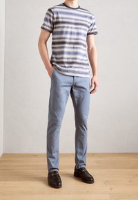 Gestreiftes Kurzarmhemd in Blau und Beige, kombiniert mit hellblauen Hosen und schwarzen Loafers. Glatter Stoff, lässige Passform und tonale Details.