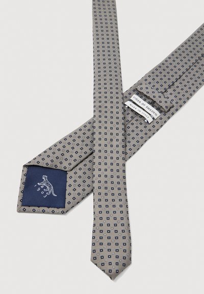 Cravat gri cu un model geometric format din pătrățele bleumarin și albe. Prezintă o căptușeală bleumarin cu un logo de tigru și eticheta brandului, fiind fabricată din mătase.