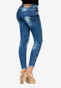 Smala jeans i medelblå denim med blekningar, fransade fållar och bakfickor; matchat med beige platåskor.