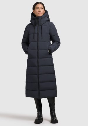 Langer, dunkelblauer Puffer-Mantel mit Kapuze, Frontreißverschluss, gestepptem Muster und Seitentaschen, kombiniert mit kniehohen schwarzen Stiefeln.
