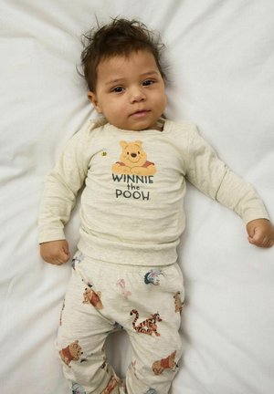 Lichtbeige pyjama-set met een Winnie the Pooh-afbeelding op de top en speelse karakters op de broek, gemaakt van zachte stof.