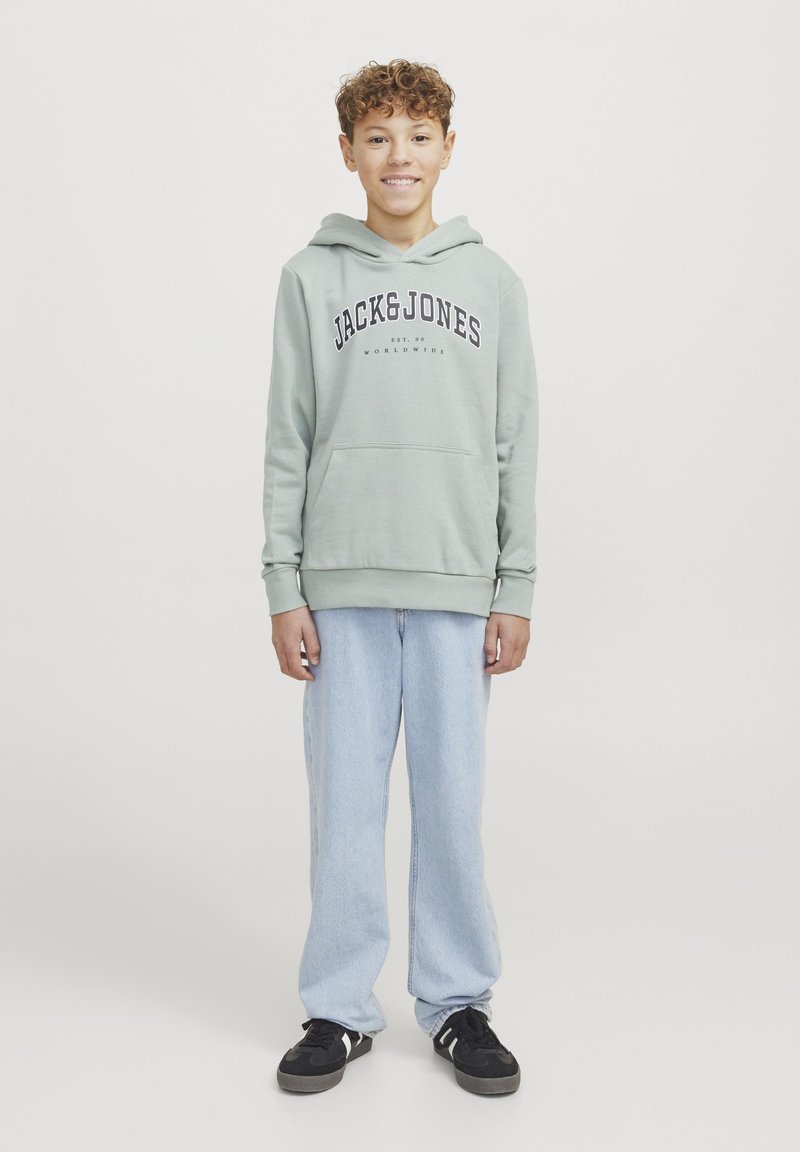 Hoodie verde chiaro con stampa "JACK&JONES", tasca a marsupio, abbinato a jeans larghi azzurri e sneakers nere.