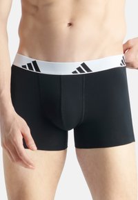 Svarta boxershorts med ett vitt elastiskt midjeband som har tre svarta diagonala ränder. Slät, åtsittande design och kort ben täckning.