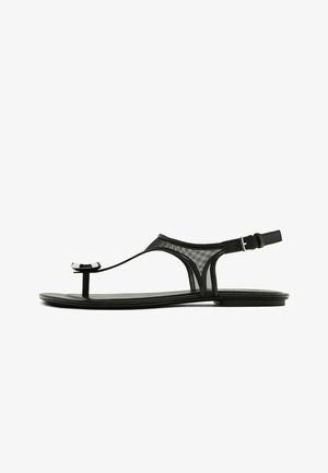 Sandali piatti neri con una cinghia in rete, un sottile anello per le dita e una fibbia regolabile alla caviglia. Presentano un design elegante e minimalista con accenti lucidi.