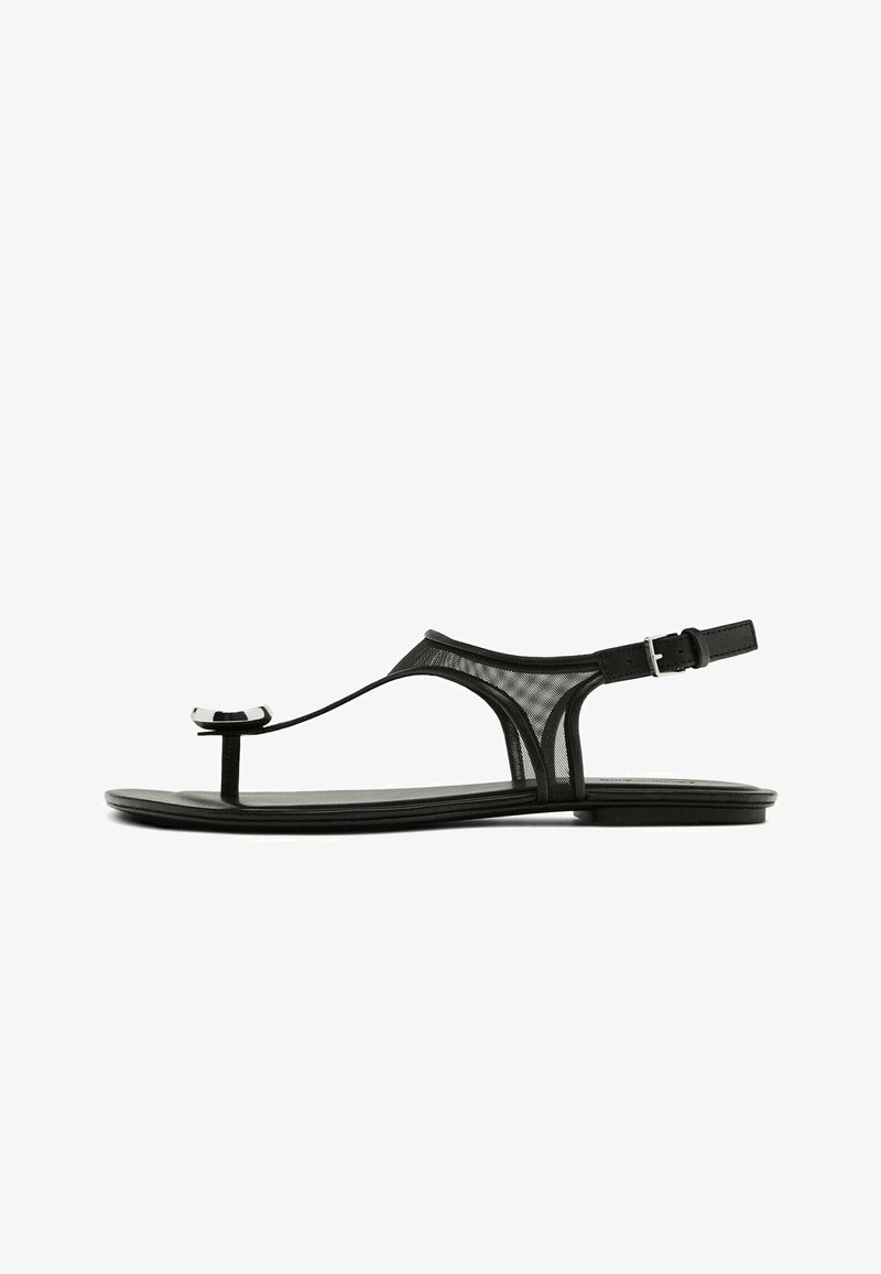 Black flat sandals with a mesh strap, thin toe loop, and adjustable ankle buckle. Features a sleek, minimalist design with shiny accents.