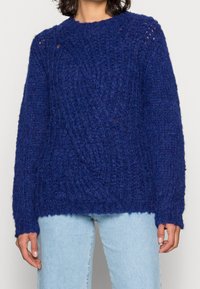 Pletený svetr v tmavě modré barvě s texturovaným vzorem, kulatým výstřihem a dlouhými rukávy. Materiál působí měkce a hrubě.