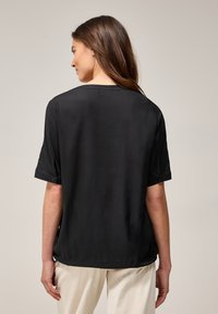Chemise noire à manches courtes avec une coupe décontractée, texture lisse et poignets repliés. Présente un col arrondi et des coutures arrière discrètes.