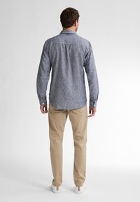 Camicia a maniche lunghe blu a quadri con colletto a bottoni, abbinata a pantaloni beige e sneakers bianche, vista da dietro.