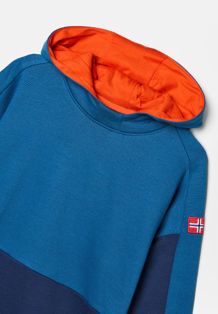 Kapuzensweatshirt in Blau und Marineblau, mit einer orangen Innenkapuze. Verfügt über einen strukturierten Stoff und ein kleines Flaggenpatch am Ärmel.