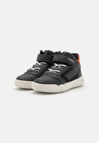 Zapatillas altas negras con parte superior de cuero liso, entresuela blanca, cordones elásticos y correa de Velcro, con detalles en color naranja y perforaciones.