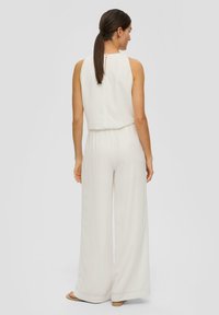 Witte mouwloze jumpsuit met een relaxte pasvorm, voorzien van een cinched taille, wijde pijpen en een keyhole detail op de rug. Gladde stoftextuur.