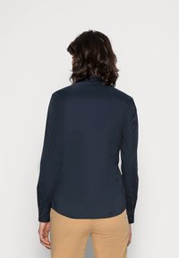 Navy long-sleeve shirt with a smooth texture and collar, featuring buttoned cuffs and a slightly curved hemline. No visible patterns.